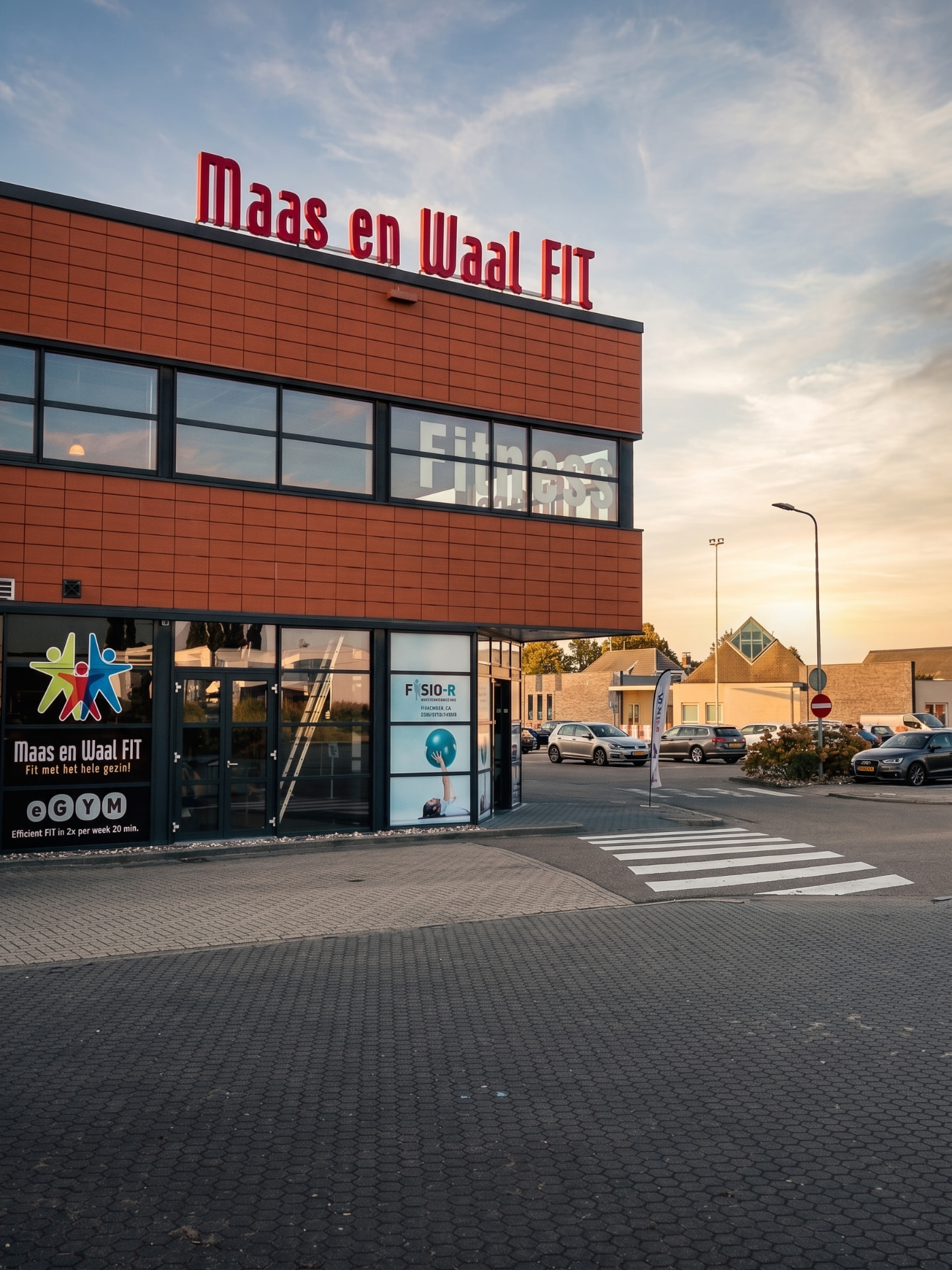Het gebouw van Maas en Waal Fit in Beneden-Leeuwen bij zonsondergang, met daarin de praktijk boven de Jumbo